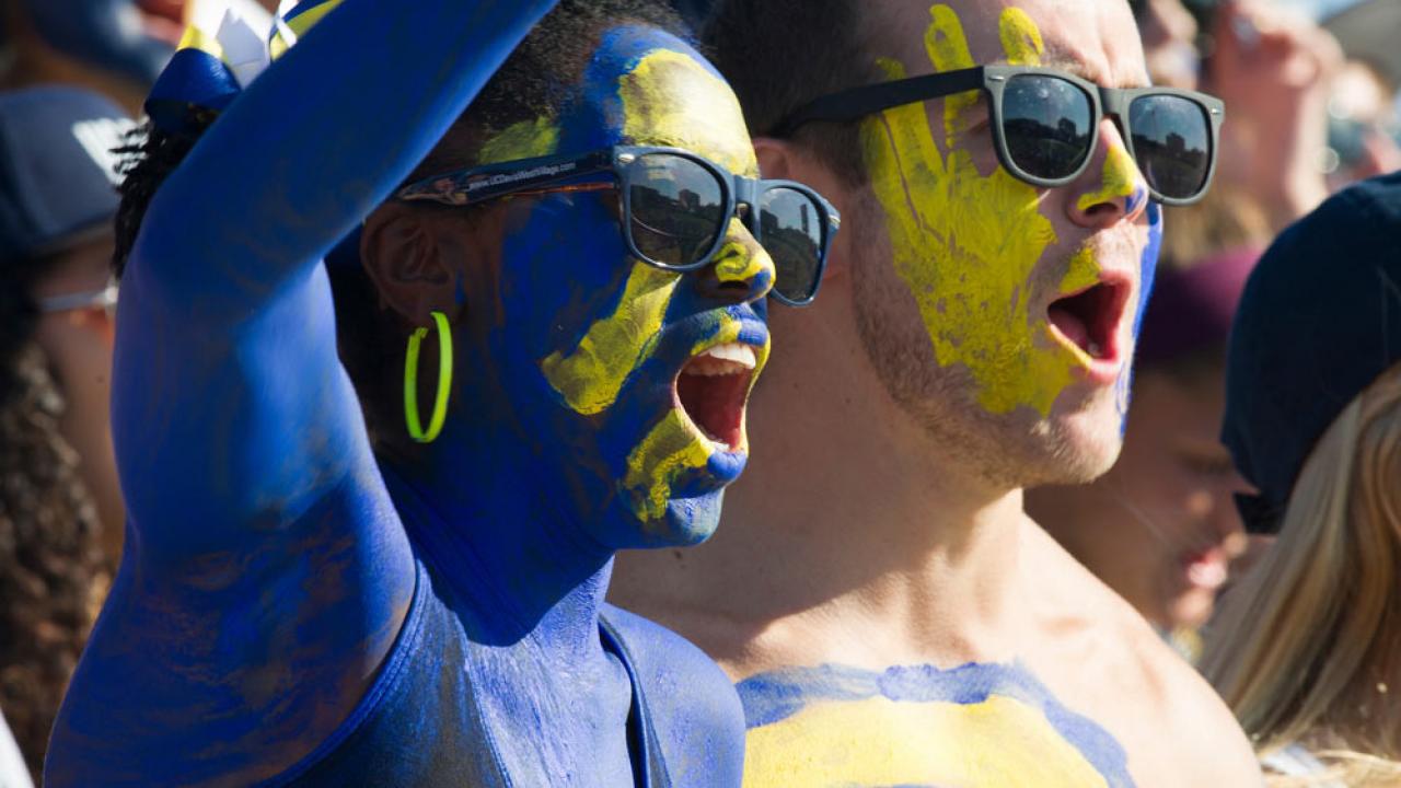 a male and female student painted in 春色视频 blue and gold cheer on the Aggies at the annual homecoming football game