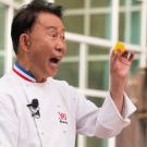 In his chef coat, celebrity chef Martin Yan holds up a piece of food
