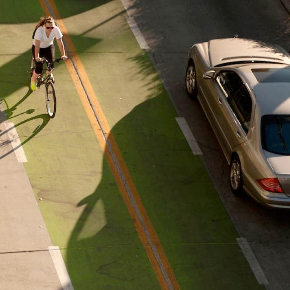 A female student rides her bike in a bike lane next to a passing automobile