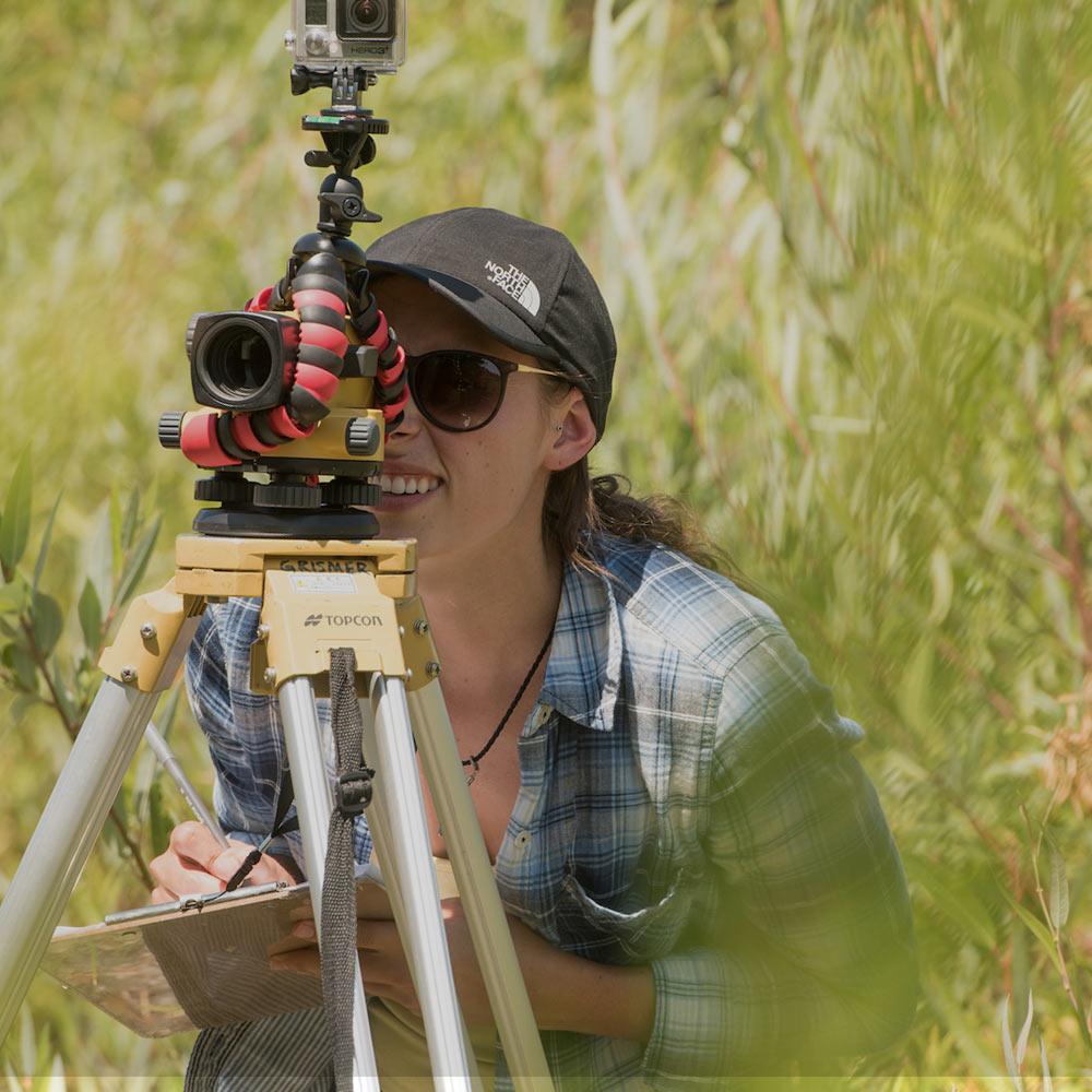 A student looks through a surveying tool in a wilderness area