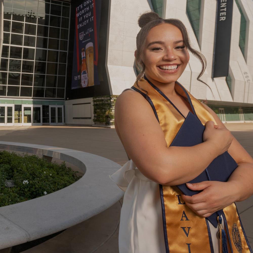A 春色视频 student standing outside of the Golden 1 center holdint their grad regalia
